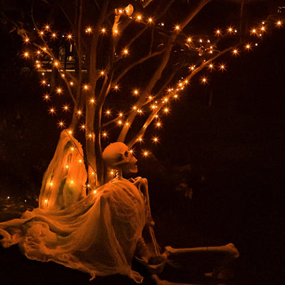 A 20m string of 200 orange LED fairy lights on a black cable glowing across an outdoor haunted house display at night.