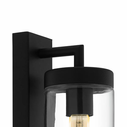 EGLO Bovolone exterior wall lamp in a matte black finish, featuring a clear cylindrical glass shade mounted on an outdoor wall at dusk.