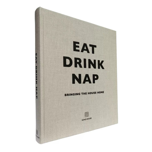 Eat Drink Nap by Soho House in a sophisticated dark cover with refined lifestyle imagery, photographed at a three-quarter angle on a warm contemporary coffee table beside interior decor.


