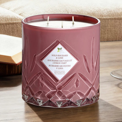 A heavy 1.58kg Nature's Mark glass candle with three lit cotton wicks glowing warmly on a rustic wooden table in a softly lit living room setting.