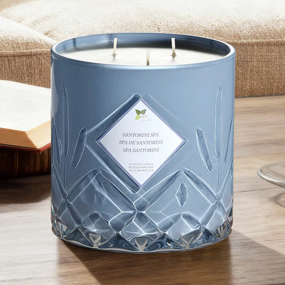 A heavy 1.58kg Nature's Mark glass candle with three lit cotton wicks glowing warmly on a rustic wooden table in a softly lit living room setting.
