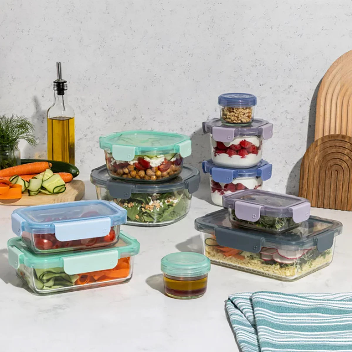 Top-down view of the 20-piece Ello Colour Lock glass food storage set arranged on a clean quartz kitchen countertop featuring clear glass bases and colorful airtight snap lids.
