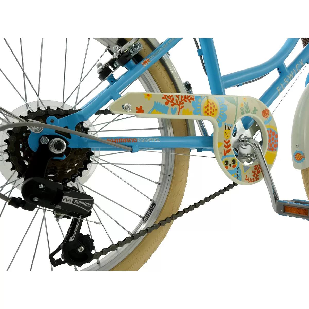 Side profile of the satin Hawaiian blue Elswick Cherish 20-inch kids heritage bike showing the front wicker basket, cream tires, and brown leather-effect saddle on a paved path.