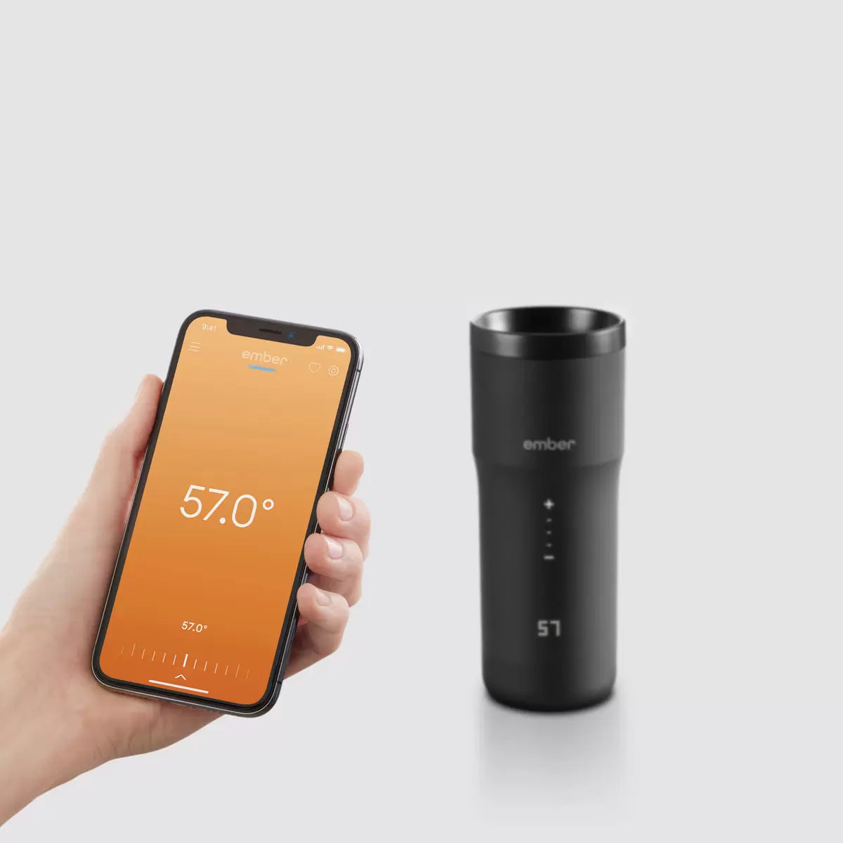Matte black Ember Temperature Control Travel Mug 2+ with illuminated digital touch display resting on its charging coaster on a wooden office desk.