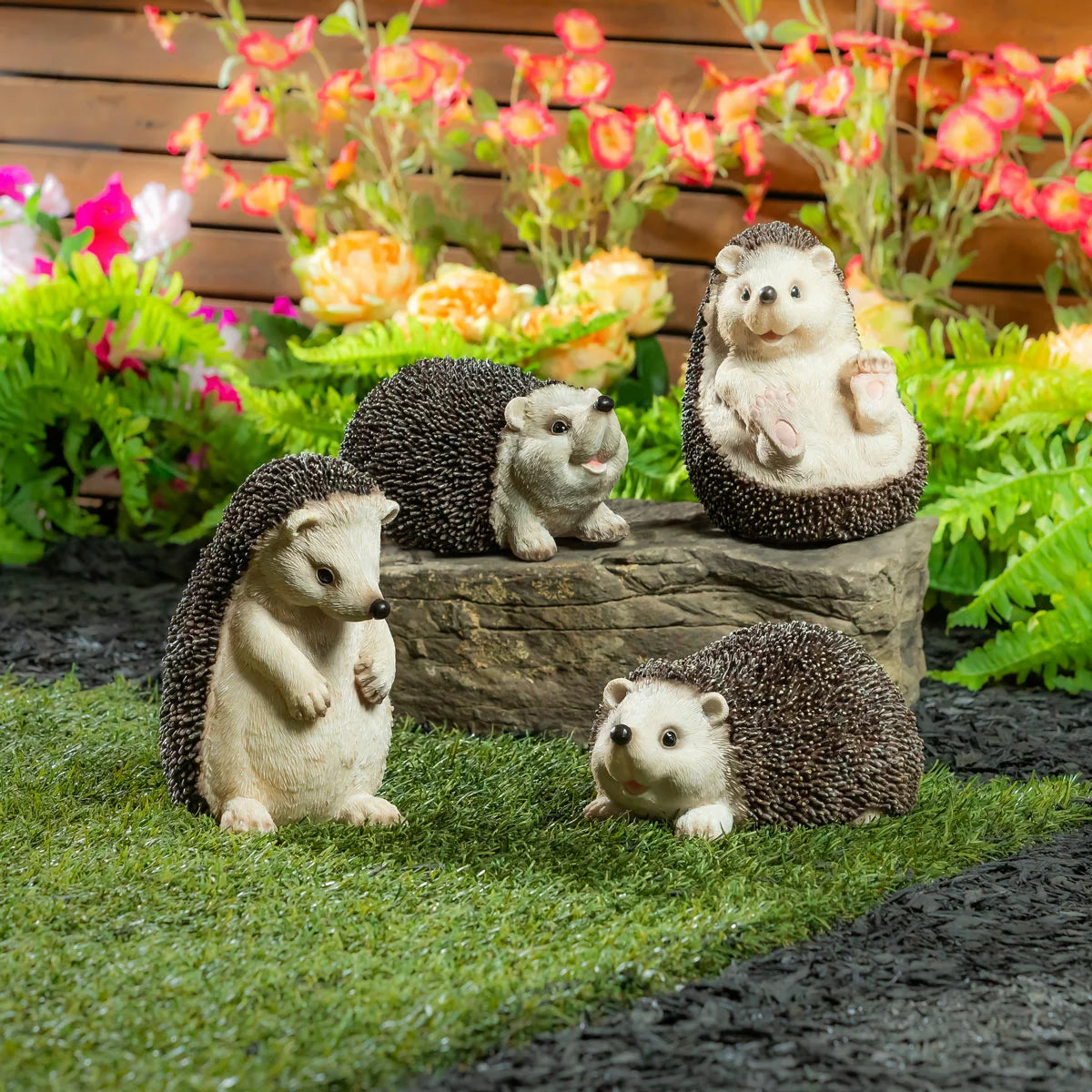 A set of realistic Evergreen Hedgehog Family Statues tucked into a green garden border with flowers.