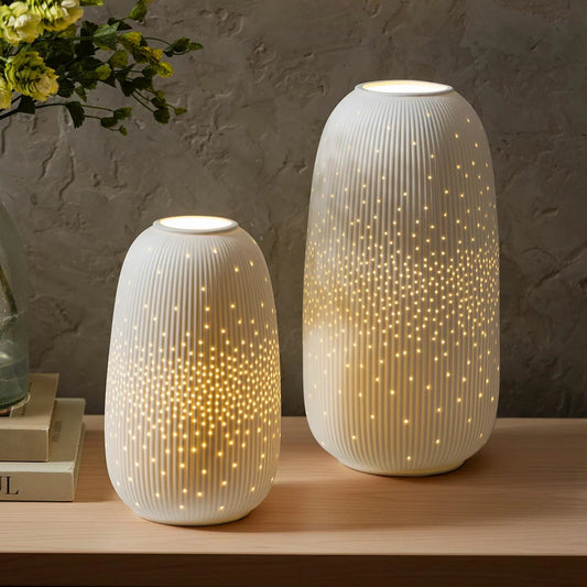 Pair of hand-shaped white and grey Evergreen porcelain LED lanterns emitting a warm glow on a minimalist wooden sideboard table.