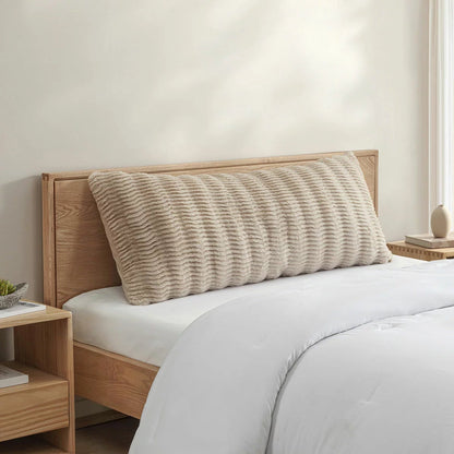 Casual Living faux fur body pillow in cream showing embossed wave texture alongside plush reverse backing on a modern bed setup.