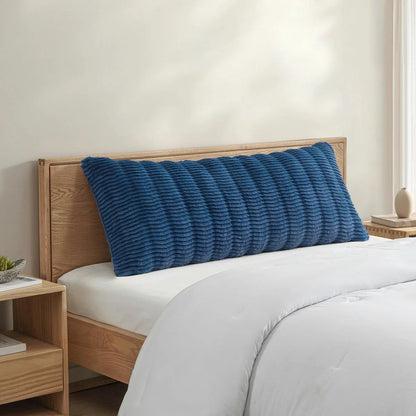 Casual Living faux fur body pillow in cream showing embossed wave texture alongside plush reverse backing on a modern bed setup.