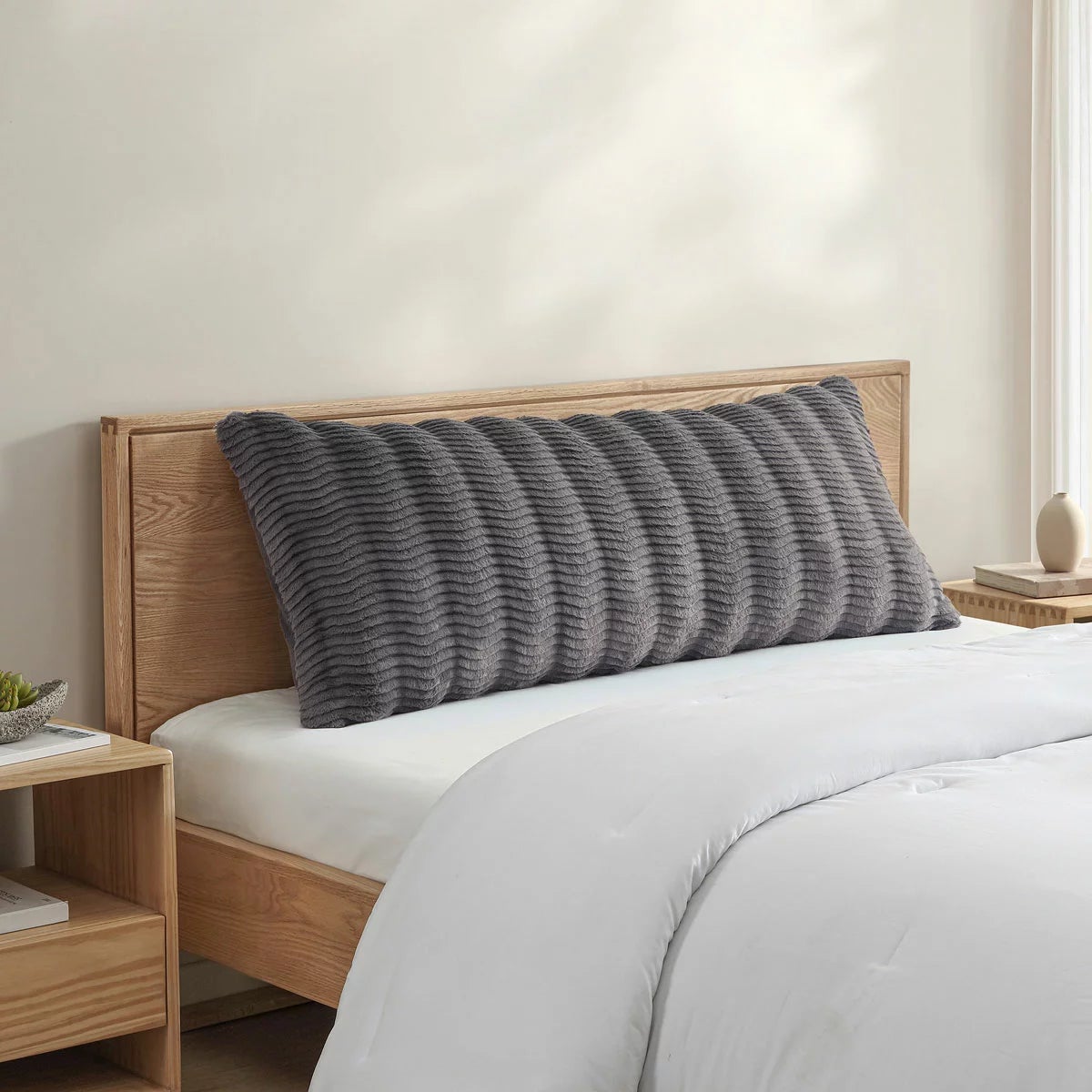 Casual Living faux fur body pillow in cream showing embossed wave texture alongside plush reverse backing on a modern bed setup.