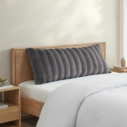 Casual Living faux fur body pillow in cream showing embossed wave texture alongside plush reverse backing on a modern bed setup.