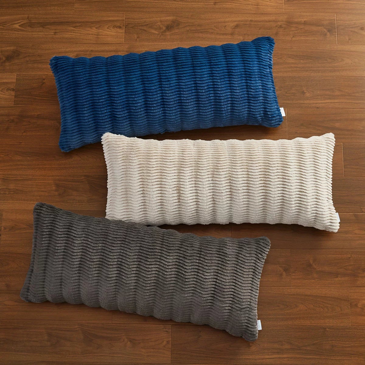 Casual Living faux fur body pillow in cream showing embossed wave texture alongside plush reverse backing on a modern bed setup.