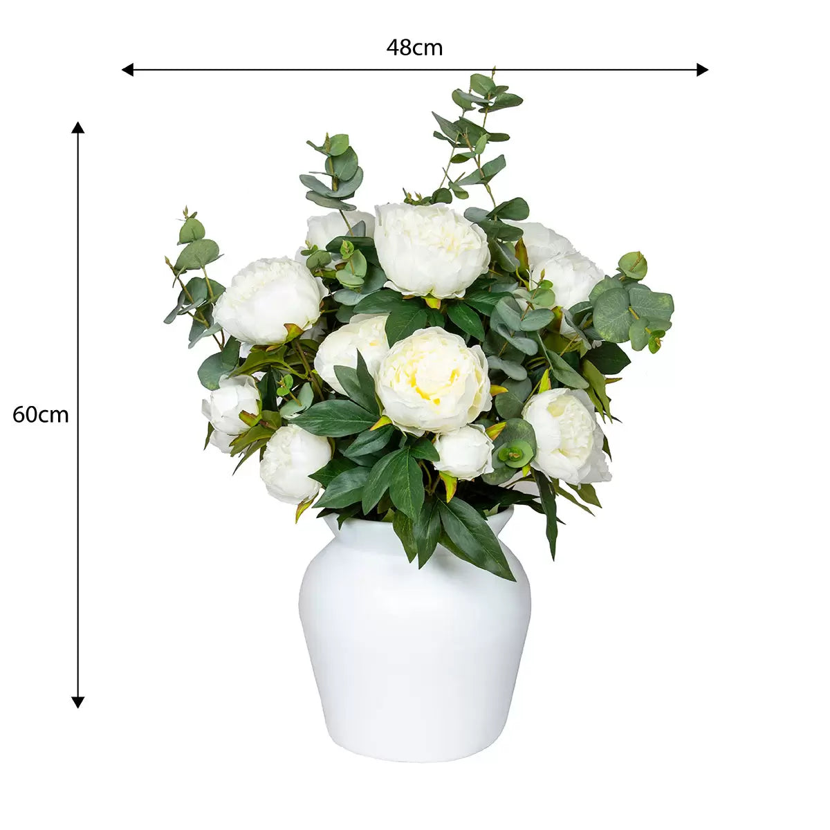Lush artificial pink peony blooms and green eucalyptus leaves arranged inside a clear glass cylinder vase sitting on a light wooden table.