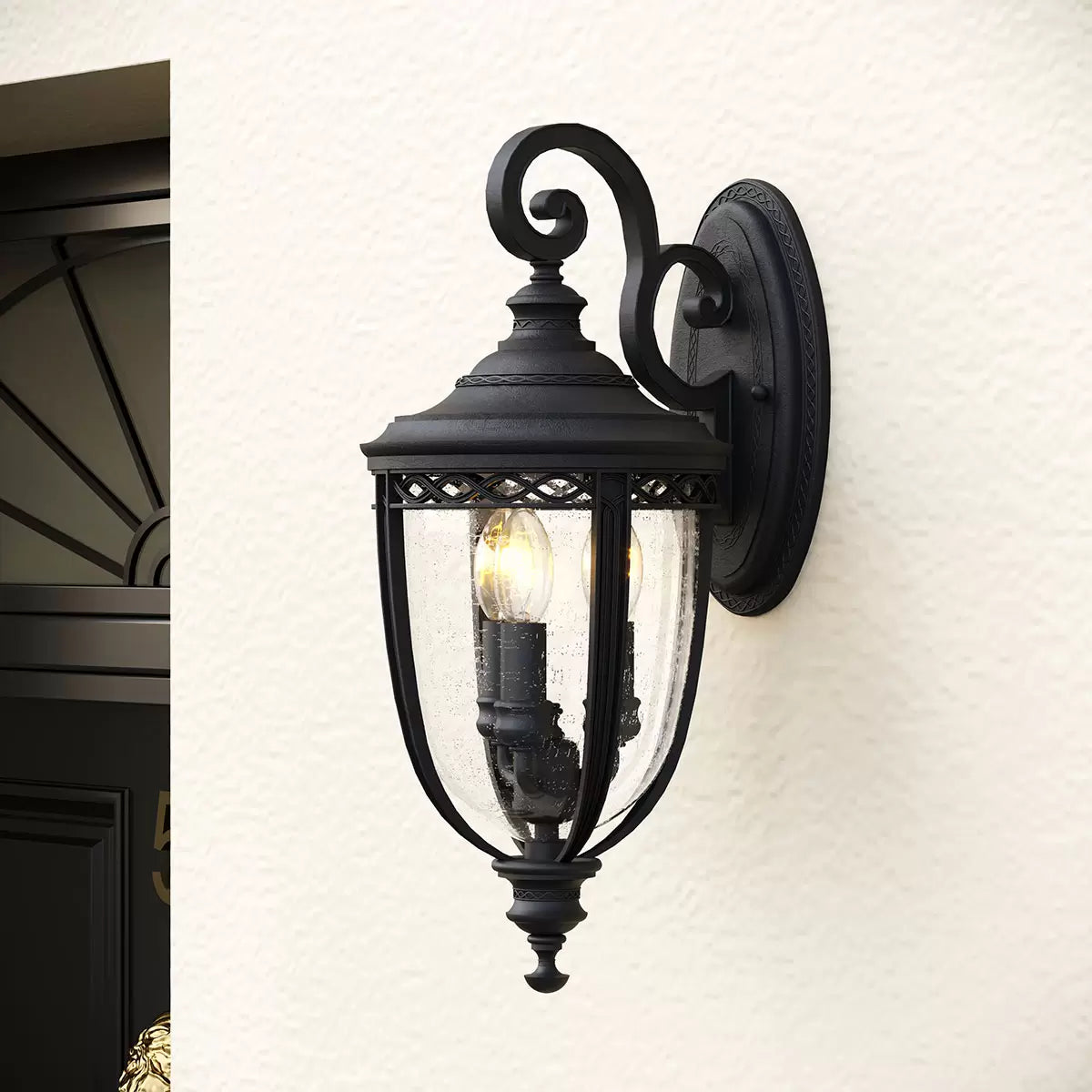A Feiss English Bridle medium wall lantern in a bronze finish with three candelabra bulbs glowing behind clear seeded glass.