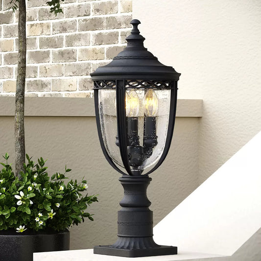 A Feiss English Bridle three-light exterior pedestal lantern with a bronze finish and seeded glass mounted on a brick pillar.