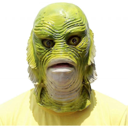 Front view of a detailed latex green fish monster mask with bulging eyes and open mouth resting on a tabletop setting.
