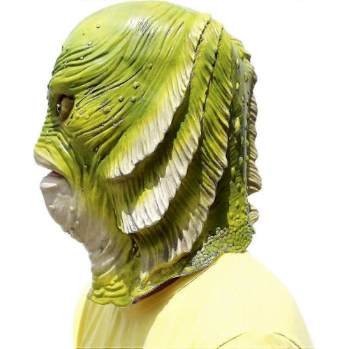 Front view of a detailed latex green fish monster mask with bulging eyes and open mouth resting on a tabletop setting.