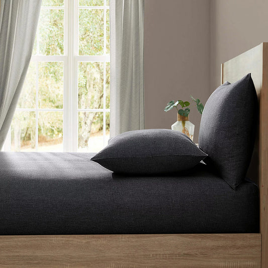 Flat lay of the Lazy Linen 100% washed charcoal flax fitted sheet neatly folded, showing the soft textured fabric finish and matching drawstring bag on a neutral backd