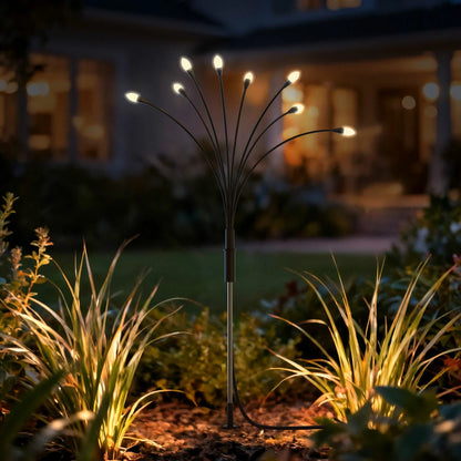 Four-pack of Fresh Source Solar Firefly Lights with warm LED bulbs installed in a lush garden flowerbed during twilight.
