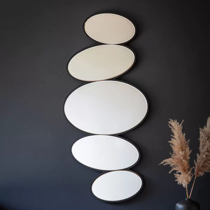 Front view of the Gallery Anderson Pebble Mirror featuring multi-segment bevelled pebble glass mounted vertically on a light grey living room wall with black wood framing.
