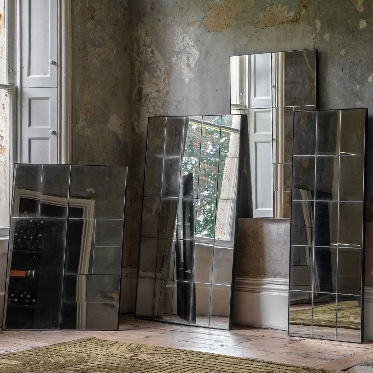 Front view of the Gallery Broadheath rectangular mirror featuring an antique distressed glass panel grid set in a black metal frame hung vertically on a neutral living room wall.