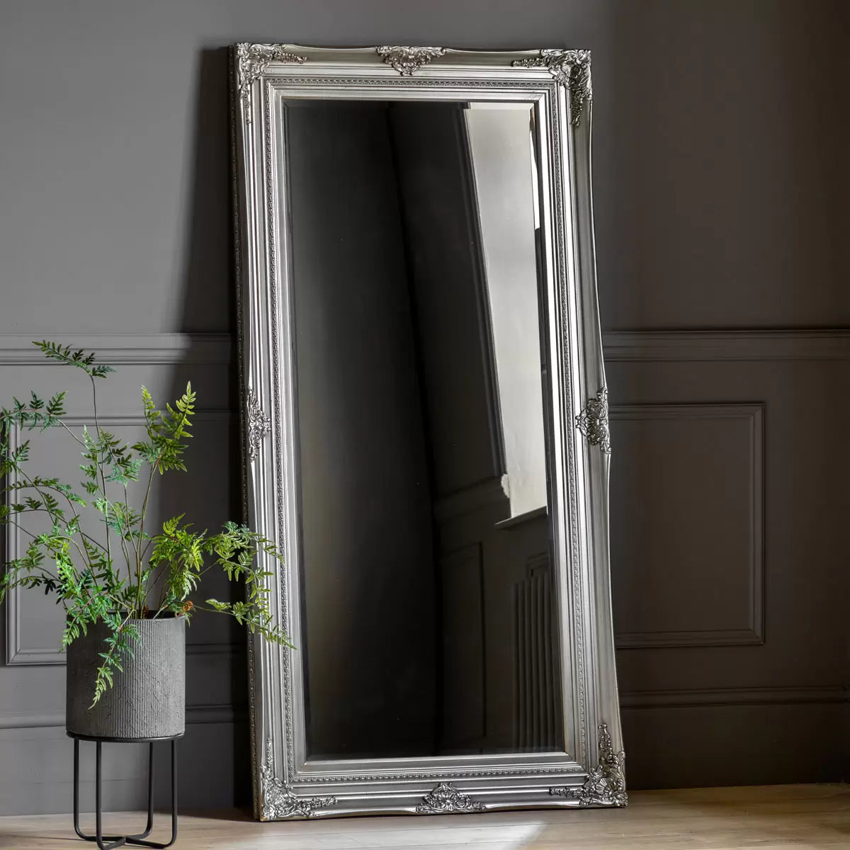 Full-length Gallery Hampshire antique silver leaner mirror with baroque wooden carved frame propped against a neutral living room wall.