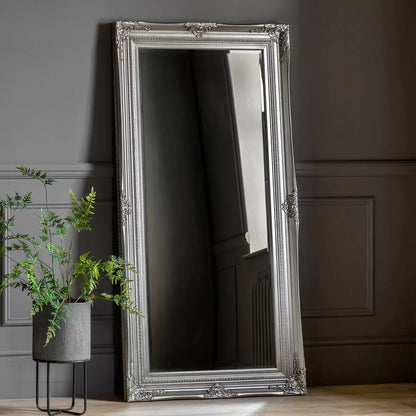 Full-length Gallery Hampshire antique silver leaner mirror with baroque wooden carved frame propped against a neutral living room wall.