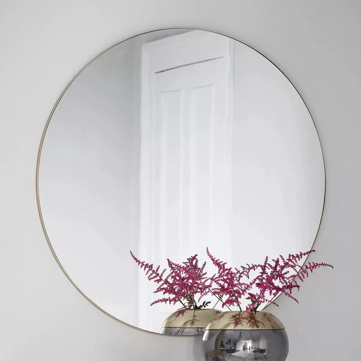 Large 100cm round wall mirror featuring a subtle champagne metal frame hanging in a brightly lit modern interior setting.