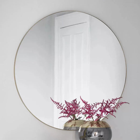 Large 100cm round wall mirror featuring a subtle champagne metal frame hanging in a brightly lit modern interior setting.