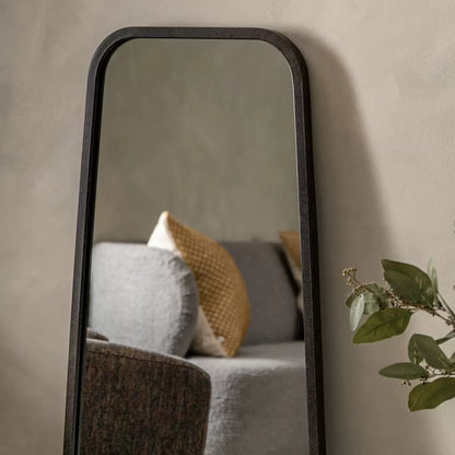 Front view of the Gallery Kurva Black Leaner Mirror measuring 56.5 by 123cm with rounded corners and a matte black metal frame leaning against a neutral living room wall.