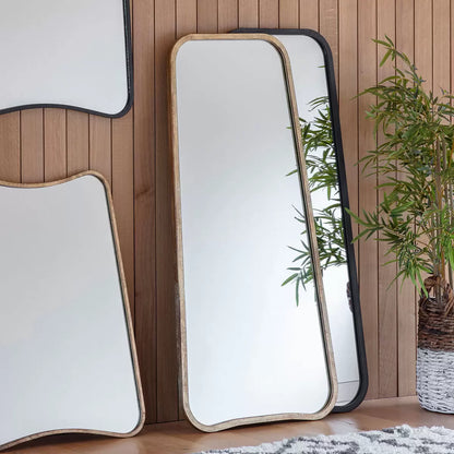 Front view of the Gallery Kurva gold metal frame leaner mirror with soft curved corners leaning against a light beige wall.