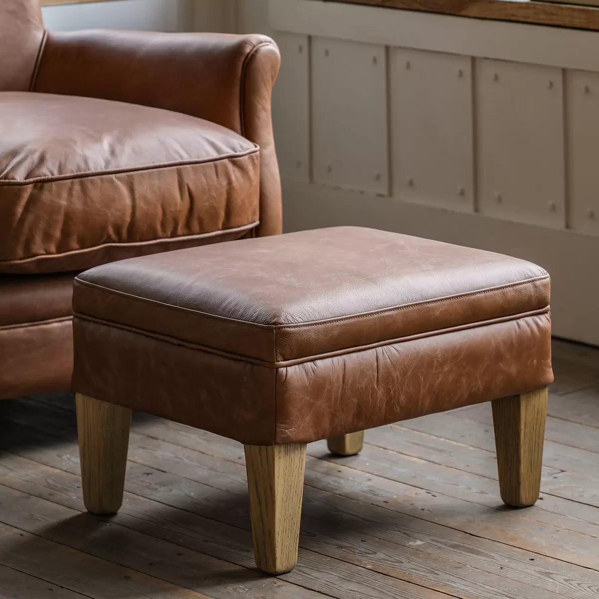 Gallery Mr. Paddington vintage brown leather footstool with plump cushion and solid ash legs in a modern living room setting.