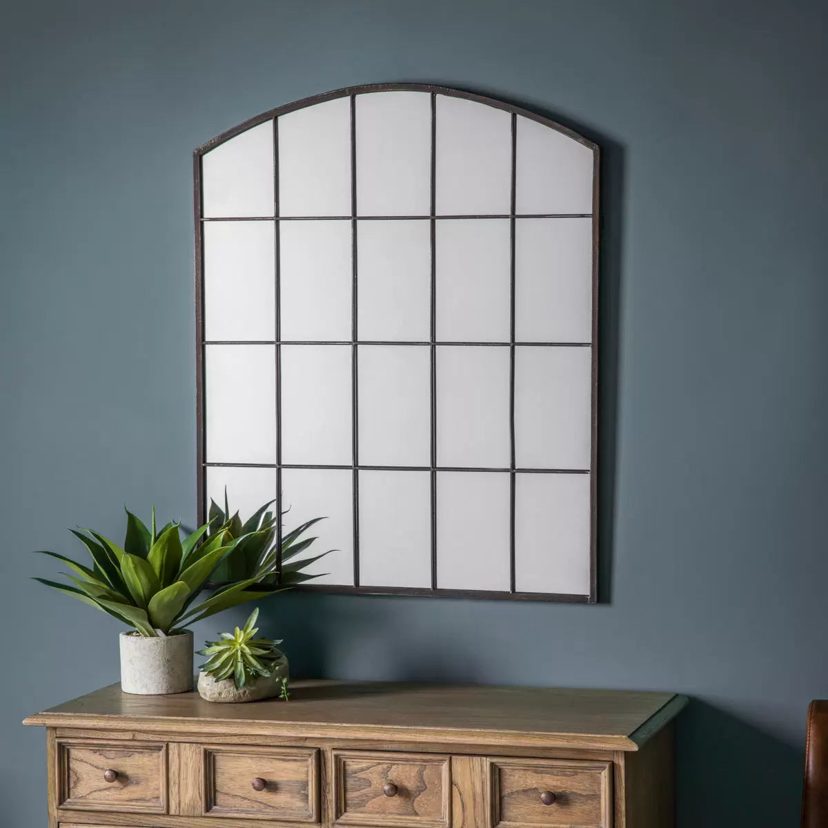 Front view of the Gallery Rockford Window Mirror with a curved iron arch frame and natural raw metal finish mounted on a neutral living room wall.