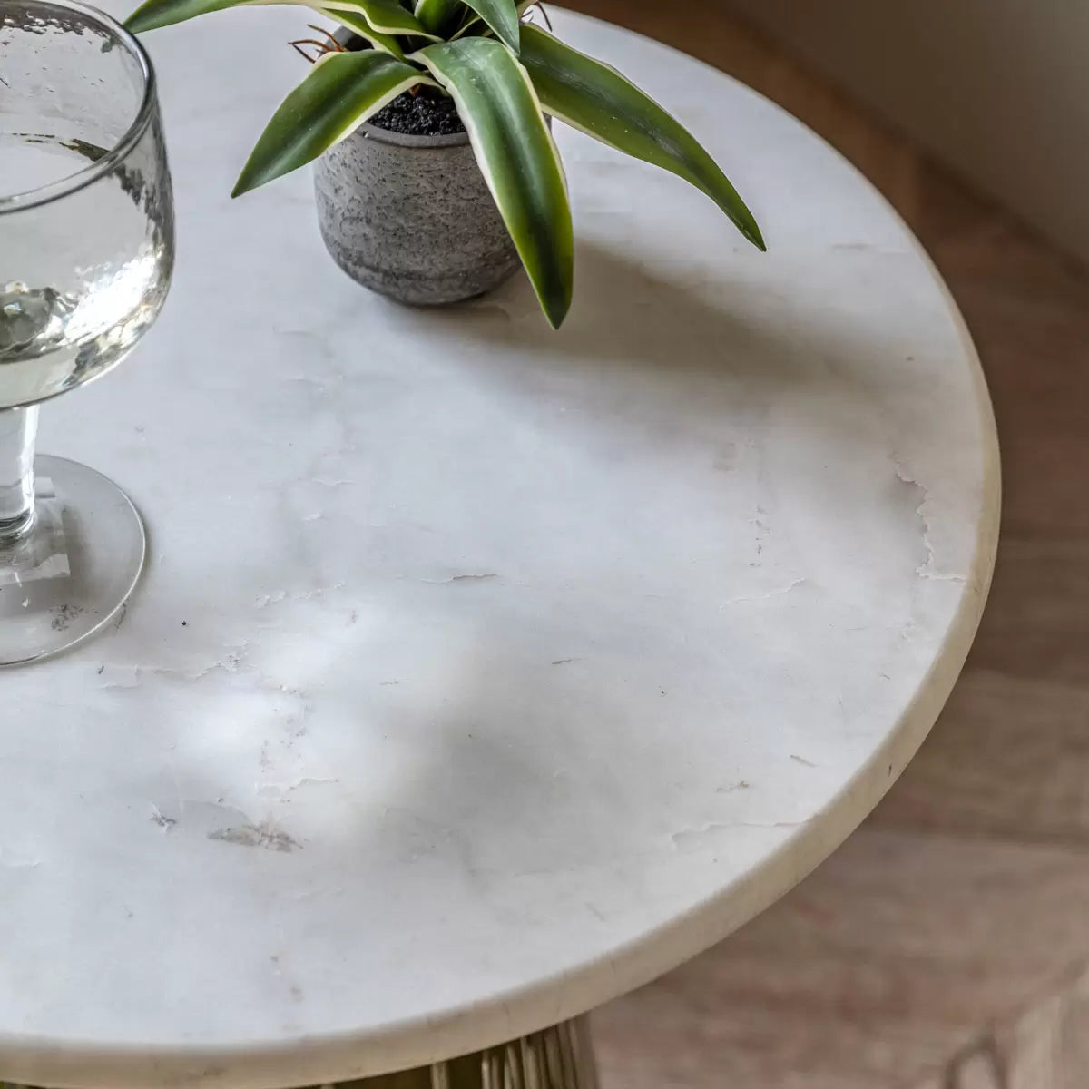 Eye-level studio shot of the Gallery Seville side table featuring a round white marble top, gold aluminium collars, and a ribbed emerald green glass base in a brightly lit modern living room.
