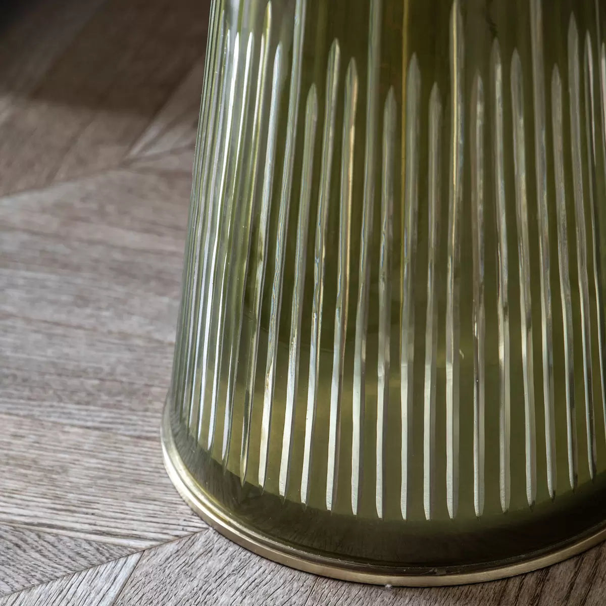 Eye-level studio shot of the Gallery Seville side table featuring a round white marble top, gold aluminium collars, and a ribbed emerald green glass base in a brightly lit modern living room.