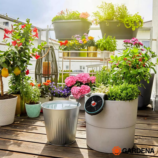 Gardena AquaBloom solar-powered irrigation unit mounted on a flower pot, watering several balcony plants via thin drip tubes.