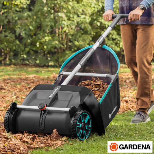 Blue and turquoise Gardena leaf and grass collector with black 90L mesh collection bag positioned on a green lawn clearing autumn leaves.