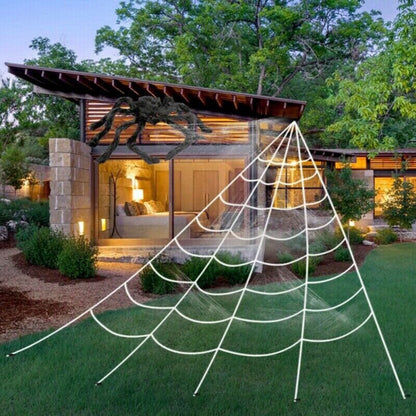 Large white 5M giant spider web stretched from a house roofline down to a grass lawn secured with ground stakes.