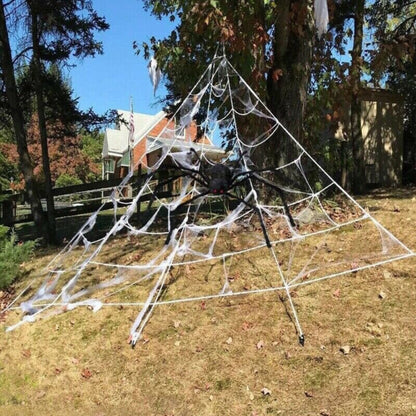Large white 5M giant spider web stretched from a house roofline down to a grass lawn secured with ground stakes.
