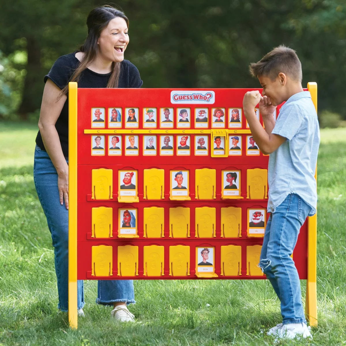 Two players sitting across from oversized red and blue Giant Guess Who? game boards on a lawn.
