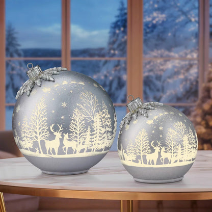 Pair of illuminated frosted glass rotating ball ornaments featuring etched reindeer and winter forest scenes glowing on a modern mantelpiece.