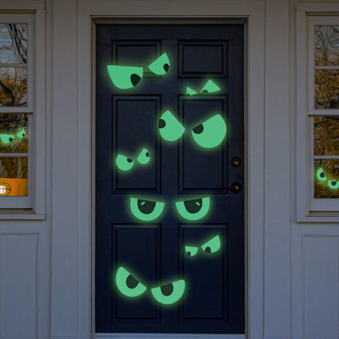 Sheet of 12 green glow in the dark spooky eye stickers arranged on a dark wooden interior door in low lighting.