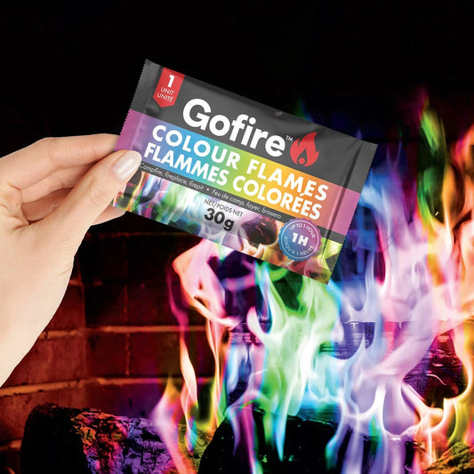 A 25 pack tube of GoFire Colour Flames sitting next to a roaring backyard fire pit displaying vibrant blue and green flames.