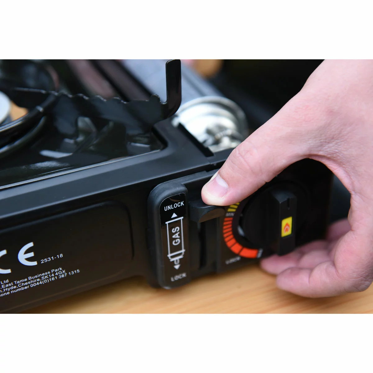 Compact black metal GoSystem Dynasty Compact II single-burner stove with serrated pan supports sitting on a wooden picnic bench next to its hardshell carrying case.