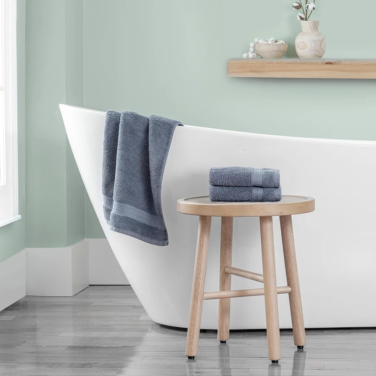 Stack of three plush 670 GSM Grandeur 100% cotton hand towels in three stylish colors neatly folded on a modern bathroom shelf.