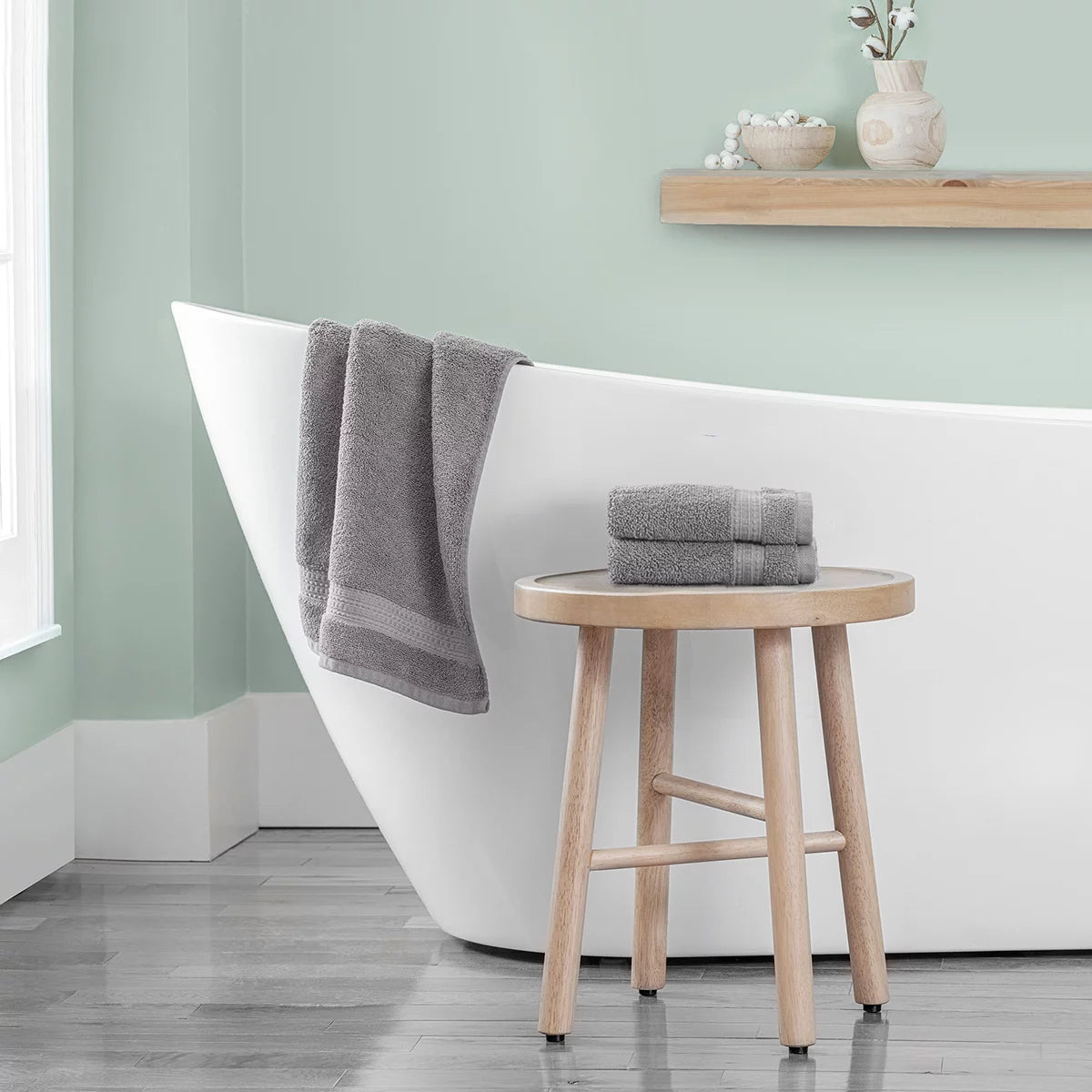 Stack of three plush 670 GSM Grandeur 100% cotton hand towels in three stylish colors neatly folded on a modern bathroom shelf.
