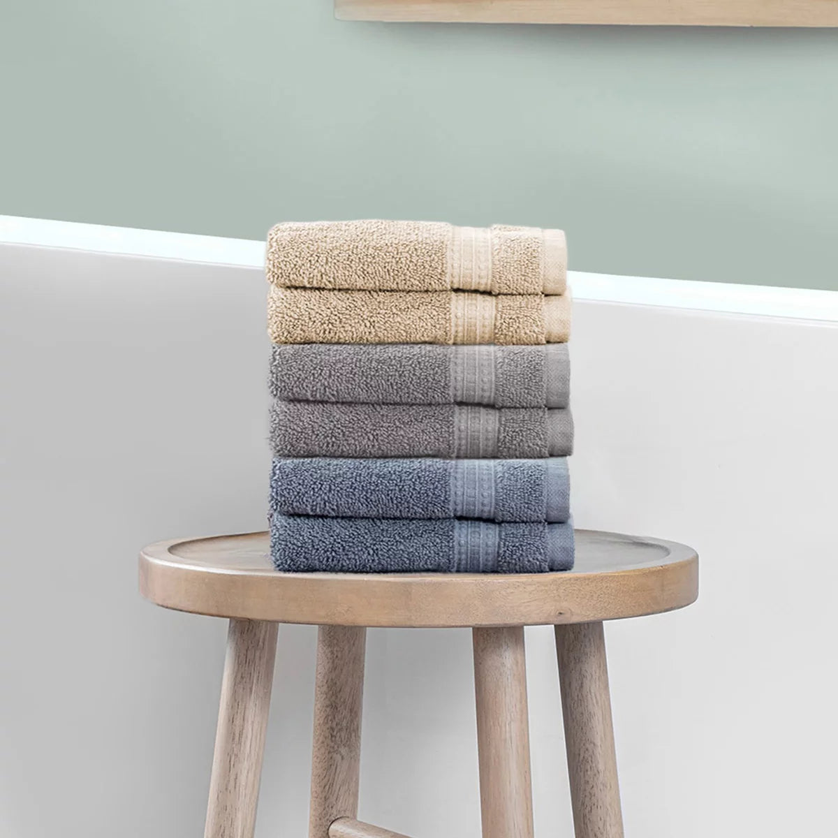 Stack of three plush 670 GSM Grandeur 100% cotton hand towels in three stylish colors neatly folded on a modern bathroom shelf.