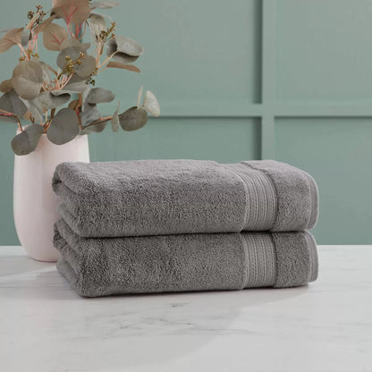Pair of thick, folded dark grey 100% HYGROCOTTON bath towels displaying dense 708 GSM pile texture stacked on a white marble vanity.