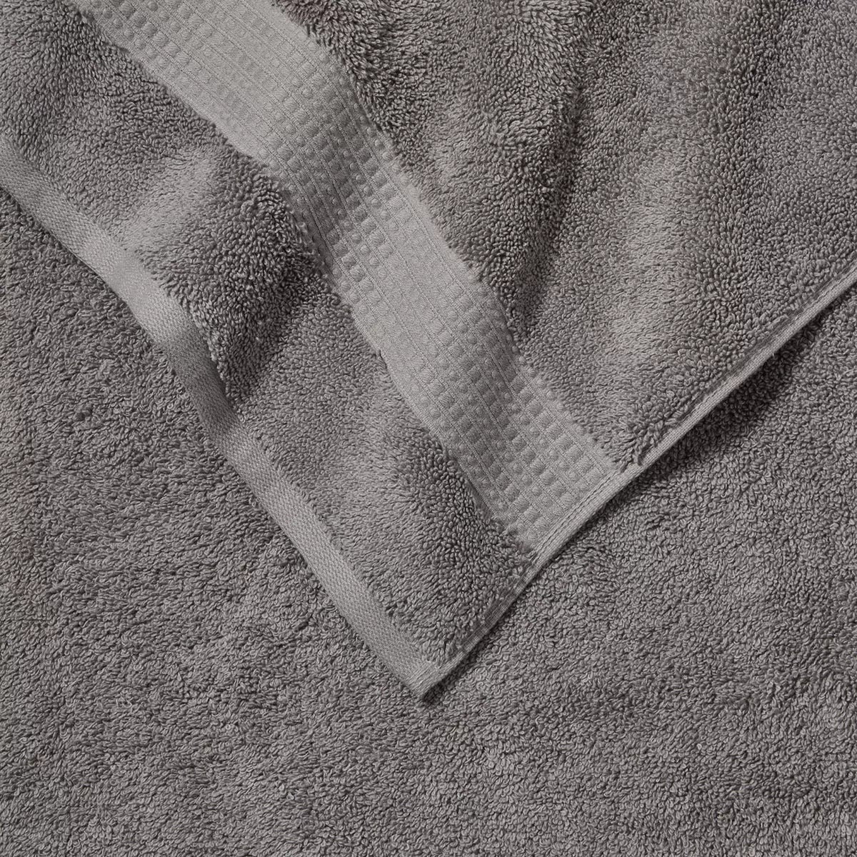Pair of thick, folded dark grey 100% HYGROCOTTON bath towels displaying dense 708 GSM pile texture stacked on a white marble vanity.