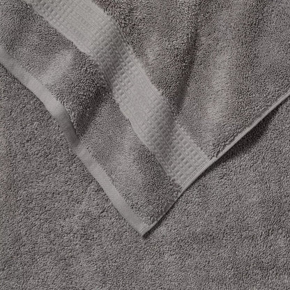 Pair of thick, folded dark grey 100% HYGROCOTTON bath towels displaying dense 708 GSM pile texture stacked on a white marble vanity.