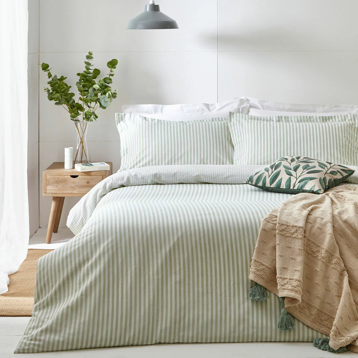 Vertical view of a single bed styled with the green and white striped Yard Hebden cotton duvet cover, displaying the reversible side folded down in a bright, modern bedroom.